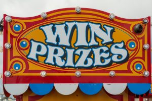 Vibrant carnival sign with marquee lights reads "WIN PRIZES" in bold blue and white letters, inviting fundraising success.